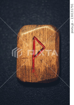 Vertical close-up of a handcrafted wooden Wunjo rune stone, featuring the carved joy symbol filled with red pigment on a rustic grain 138131791