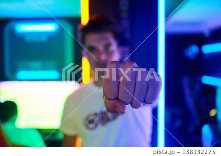 Young Gamer Punching Fist Toward Camera in Neon Arcade With Confident Gesture and Vivid Lighting Young Gamer Punching Fist Toward Camera in Neon Arcade With Confident Gesture and Vivid Lighting 138132275