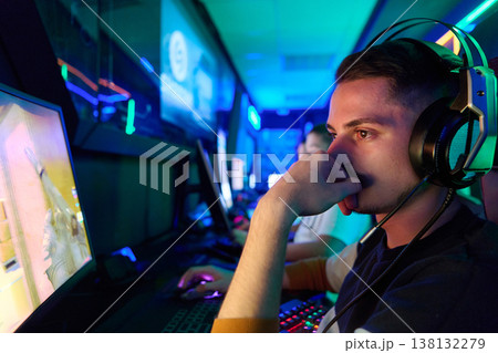 Focused Young Gamer Wearing Headset Competing in Neon-Lit Esports Arena During Intense PC Match 138132279