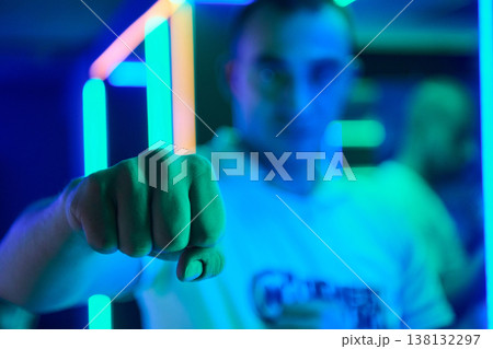 Young Man Showing Fist Toward Camera in Neon Blue Nightclub With Colorful LED Lights 138132297