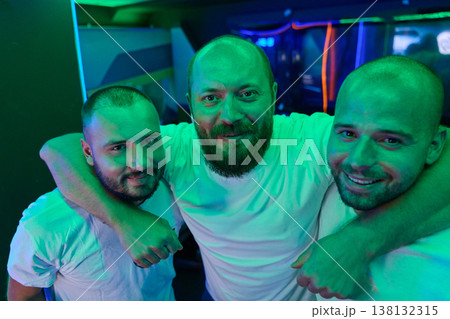 Three Male Friends Hugging and Smiling at Neon-Lit Nightclub Party 138132315