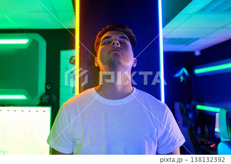 Young Gamer Relaxing Against Neon Pillar in LED-Lit Gaming Room With Cyberpunk Mood 138132392