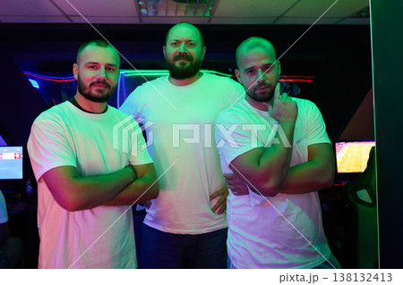 Three Male Friends and Gamers Posing Together in Neon-Lit Gaming Room With Casual White T-Shirts 138132413