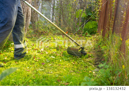 Grass trimmer cutting tall grass in the garden, close up view of a brushcutter for yard work, property maintenance and landscaping concept. 138132432