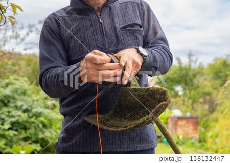 Man changes trimmer line for a string trimmer. Gardener does maintenance for gardening tool. Lawn care and yard work concept. 138132447