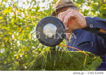 A man clears head of grass trimmer from residual grass. Gardener maintaining yard with power tool. Home improvement and lawn care equipment concept. close up view 138132449