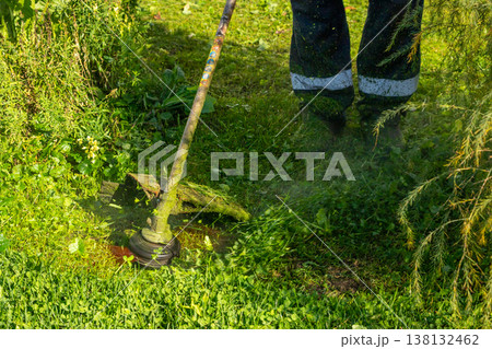 Man using grass trimmer to cut lawn in backyard. Gardener operating string trimmer to maintain greenery. Lawn care equipment, landscaping tool and grass maintenance gardening concept. Man using grass trimmer to cut lawn in backyard. Gardener operating string trimmer to maintain greenery. Lawn care equipment, landscaping tool and grass maintenance gardening concept. 138132462