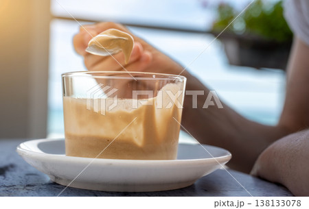 Person savoring creamy coffee mousse with a spoon at an outdoor cafe table, enjoying a refreshing sweet treat in bright daylight relaxed summer indulgence and leisure moment 138133078