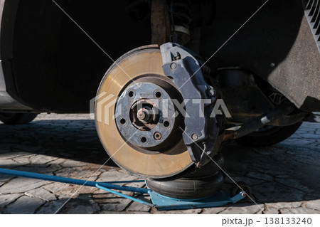 A car brake disc with visible rust and dust, mounted on a vehicle lifted by a jack. Brake caliper 138133240