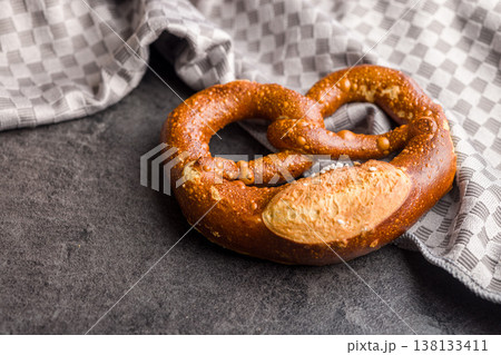 Traditional Soft Pretzel With Coarse Salt On Dark Stone Surface Beside Kitchen Towel 138133411
