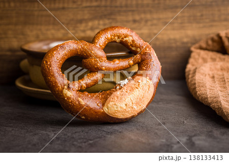 Rustic Soft Pretzel With Coarse Salt on Dark Surface Next to Ceramic Bowl and Towel Rustic Soft Pretzel With Coarse Salt on Dark Surface Next to Ceramic Bowl and Towel 138133413