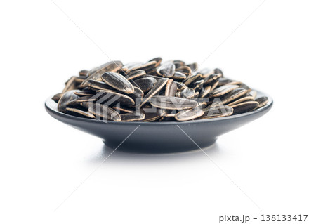 Close-Up Of Sunflower Seeds In A Black Bowl With Pile Of Seeds On White Background Close-Up Of Sunflower Seeds In A Black Bowl With Pile Of Seeds On White Background 138133417