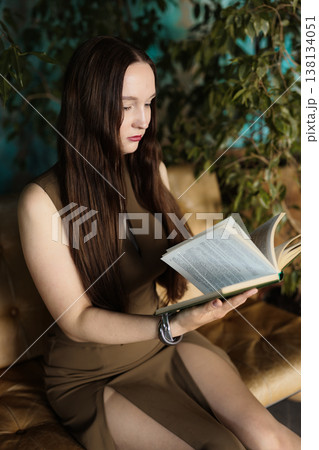 Caucasian lady gazing pensively with open book on cozy sofa environment 138134051