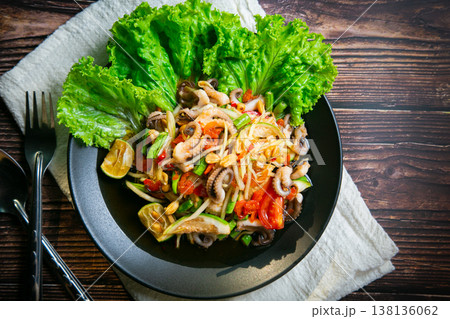 Delicious papaya salad or Tum Thai with squid tentacles, Lentils, nuts, raw papaya, fish sauce, sugar, tomato, and lime. Cutlery is placed on the wooden floor. Taken in a photo studio. Thai food. 138136062