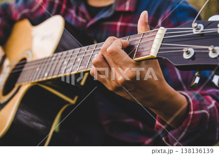 Asian lesbian in tartan shirt-wearing headset and playing guitar of string song on gold rice field with sunset light evening. close up 138136139
