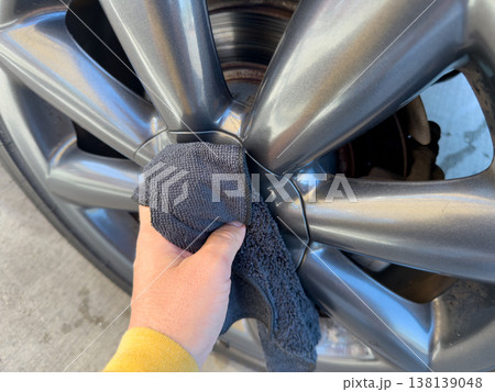 Man wiping and drying car with grey microfiber rag outdoors, closeup 138139048