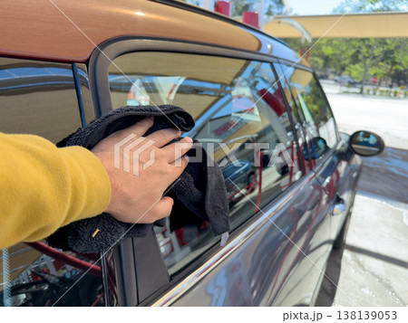 Man wiping and drying car with grey microfiber rag outdoors, closeup 138139053