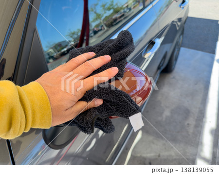Man wiping and drying car with grey microfiber rag outdoors, closeup 138139055