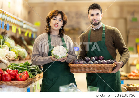 Young male and female sellers posing in grocery market holding cauliflower and plums Young male and female sellers posing in grocery market holding cauliflower and plums 138139756