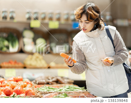 Girl in vegetable store choose carrot. 138139848