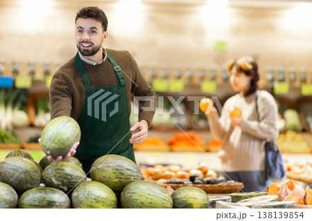 Man seller in grocery vegetable shop arrange melon. 138139854