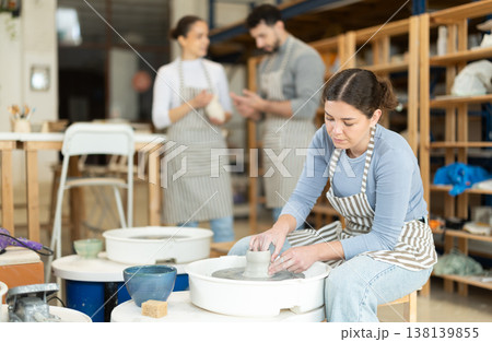 Woman in ceramics workshop with pottery wheel and various clay vessels 138139855