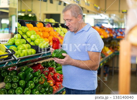 Busy old casual man pushing shopping cart and buying local bell peppers in grocery shop 138140040
