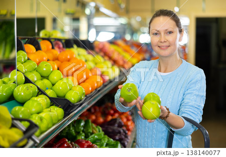 Middle-aged woman purchaser buying fresh apples in grocery store Middle-aged woman purchaser buying fresh apples in grocery store 138140077