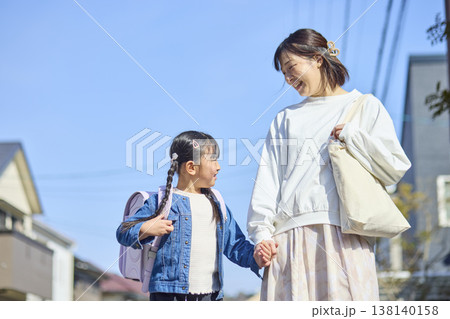 住宅街を手を繋いで歩く母親とランドセルを背負った女の子 138140158