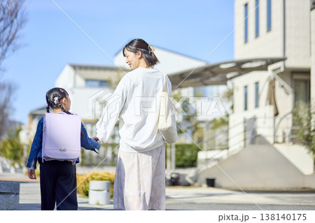 通学路で顔を見合わせ手をつなぐ小学生の女の子と母親 通学路で顔を見合わせ手をつなぐ小学生の女の子と母親 138140175