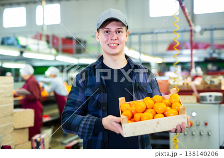 Smiling young worker with box of mandarins at sorting line Smiling young worker with box of mandarins at sorting line 138140206
