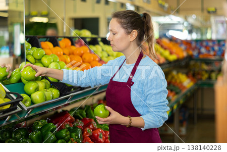 Middle-aged saleswoman putting apples on food stall in grocery store 138140228
