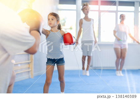 Girl with her trainer father at gym. Boy wearing boxing gloves exercise and punch to pads for boxing Girl with her trainer father at gym. Boy wearing boxing gloves exercise and punch to pads for boxing 138140389