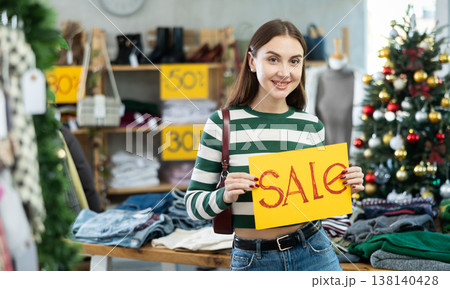 Woman with a yellow poster on sale against the background of a Christmas tree Woman with a yellow poster on sale against the background of a Christmas tree 138140428