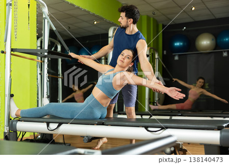 Woman doing abdominal exercises with the help of a male trainer and a reformer Woman doing abdominal exercises with the help of a male trainer and a reformer 138140473