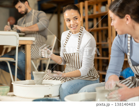 Girl working at pottery wheel and talking to girl 138140483