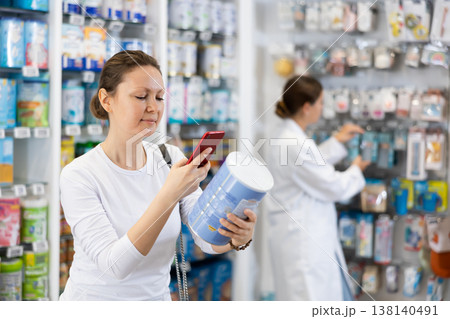 At pharmacy, woman buyer photographs packaging with infant formula. 138140491