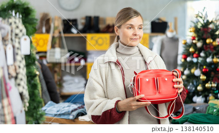 Positive young woman choosing handbag in clothing store 138140510