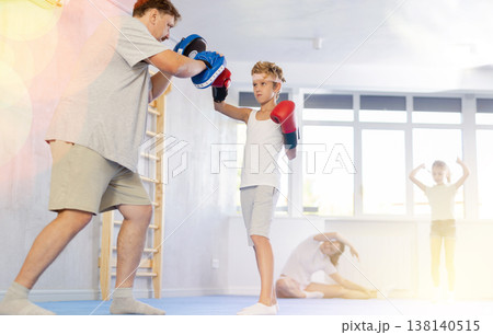 Boy and dad are boxing in gym, father helps child to work out force of blow. 138140515