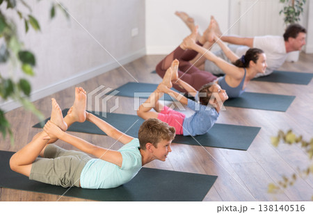 Diligent preteen boy practicing bow pose of yoga with his family 138140516