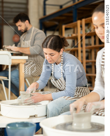 Two girls craftspersons busy molding clay products on pottery wheel Two girls craftspersons busy molding clay products on pottery wheel 138140525