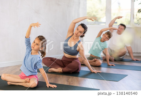 Confident mom, dad, son, and daughter sit in Padmasana and do body tilt to side Confident mom, dad, son, and daughter sit in Padmasana and do body tilt to side 138140540
