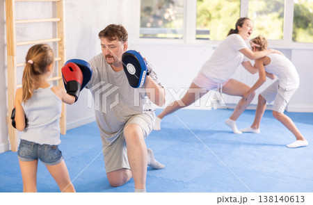 Girl and dad are boxing in gym, father helps child to work out force of blow. 138140613