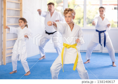 Preteen boy in kimono practicing punches as part of kata with family Preteen boy in kimono practicing punches as part of kata with family 138140617