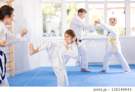 Preteen girl in kimono practicing karate kicks during sparring with mother Preteen girl in kimono practicing karate kicks during sparring with mother 138140643