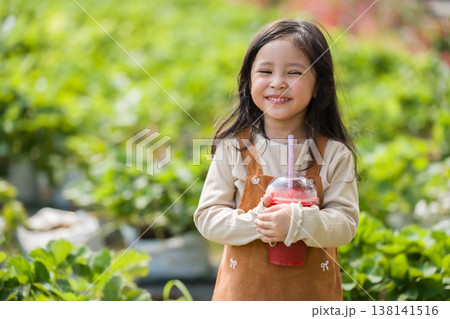 happy preschool child girl holding a cup of fresh strawberry smoothie in farm happy preschool child girl holding a cup of fresh strawberry smoothie in farm 138141516