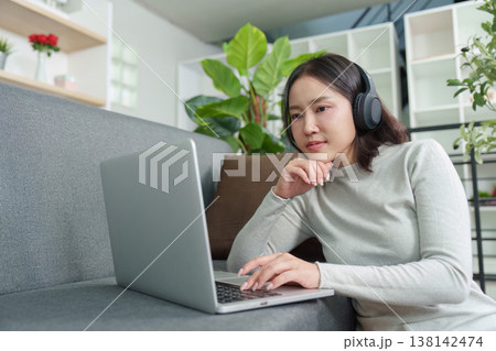 Woman working on laptop with headphones in modern living room Woman working on laptop with headphones in modern living room 138142474