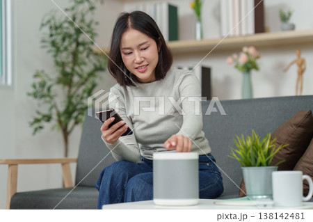 Woman using smartphone and smart speaker in modern living room 138142481