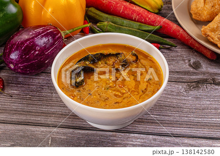 Spicy Indian lentil curry, dal tadka, in a bowl on a wooden background with fresh ingredients. 138142580
