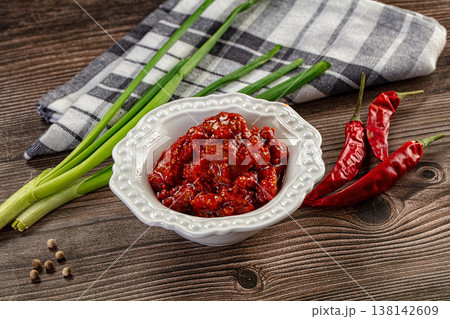 Spicy red chili pickle in a white bowl on a rustic wooden table with fresh ingredients 138142609